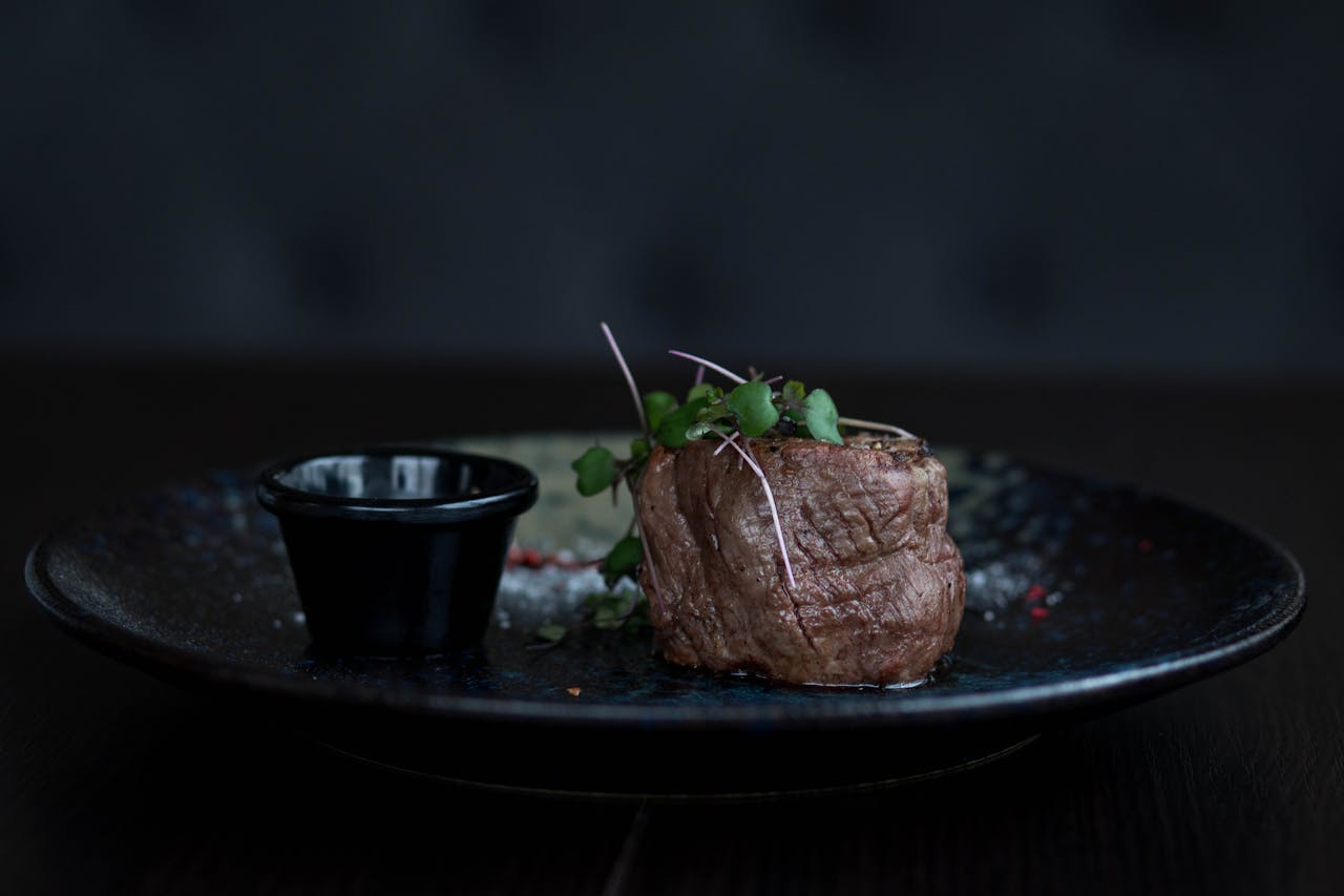 A gourmet beef filet topped with fresh herbs on a black plate, perfect for fine dining experiences.