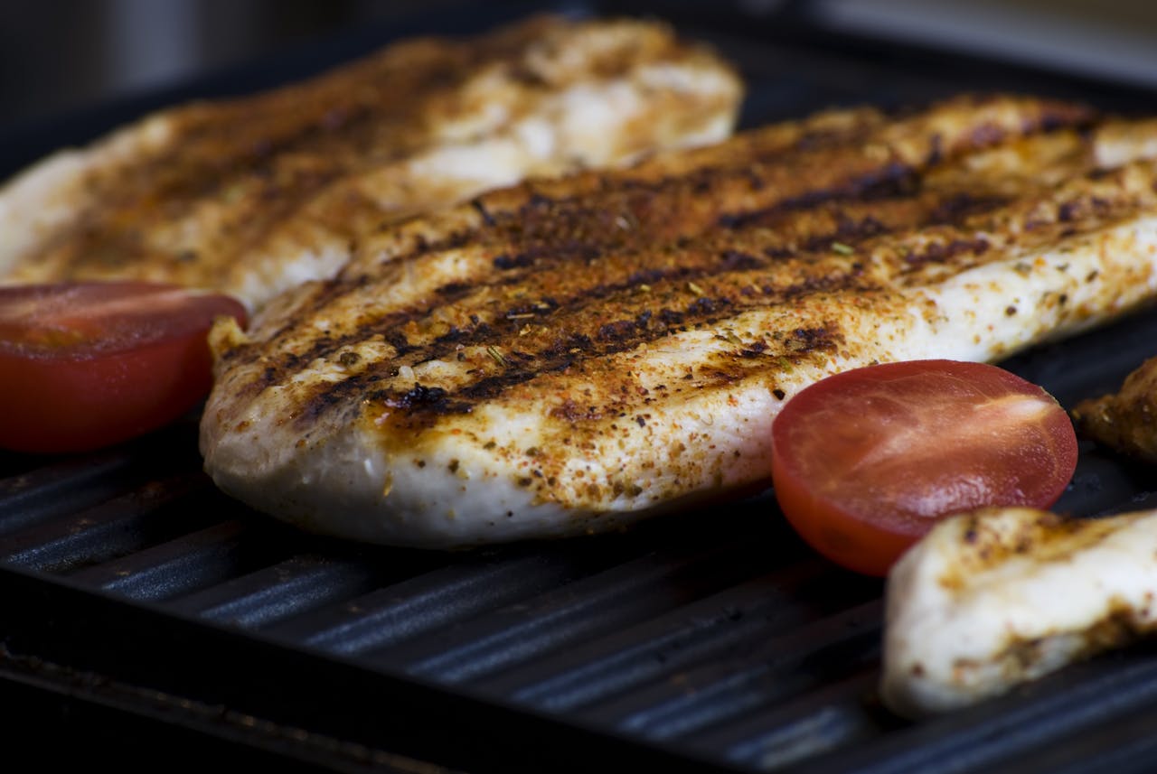 Close-up of grilled chicken breasts with tomatoes sizzling on a barbecue grill, perfect for a delicious meal.