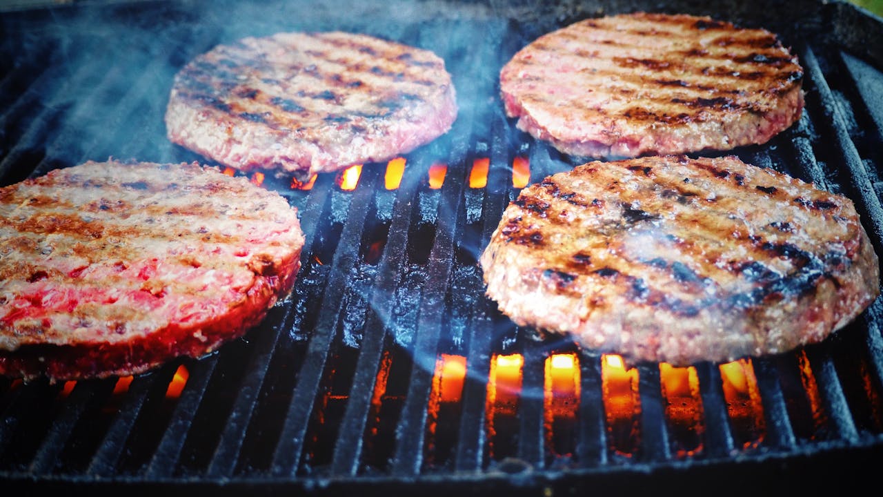 Juicy beef patties cooking on a hot grill, perfect for barbecue cookouts.